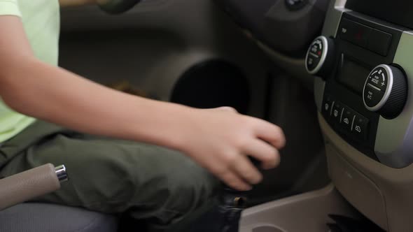 A Little Boy Sits Behind the Wheel in a Car and Shifts Gears on the Gearbox
