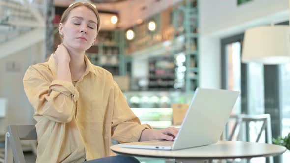 Young Woman with Neck Pain Using Laptop in Cafe 