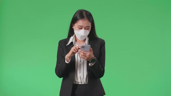 Asian Business Woman Wearing Mask Using Mobile Phone While Walking On Green Screen In The Studio