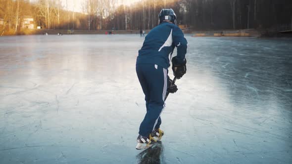 Ice Hockey Player Training with Dribbling on Frozen Lake, Professional Man Athlete Outdoor Sunset
