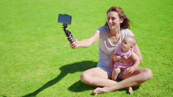 Mother Blogger with Little Daughter Having Fun Records a Video Blog on Green Grass