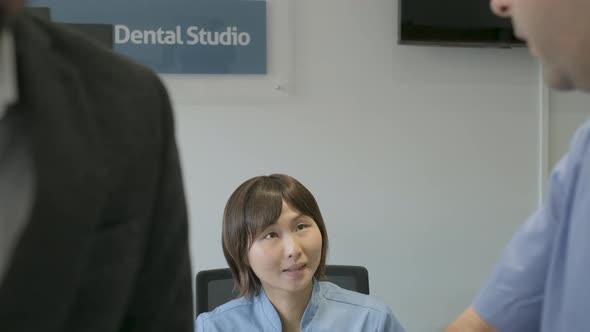 Dentist speaking with patient, assistant giving notebook to dentist