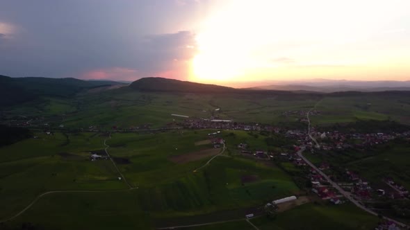 wide aerial shot of a great sunset over wide fields and green meadows near a downside, Transylvania,