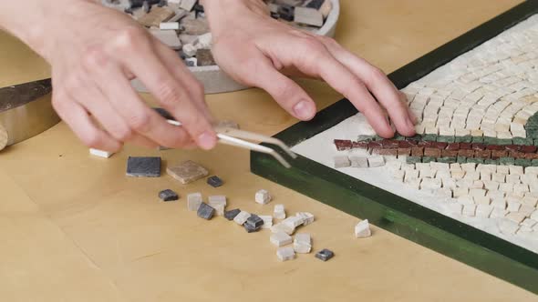 Male Hands Create Mosaics Pattern Using Tweezers and Small Pieces of Granite Stone