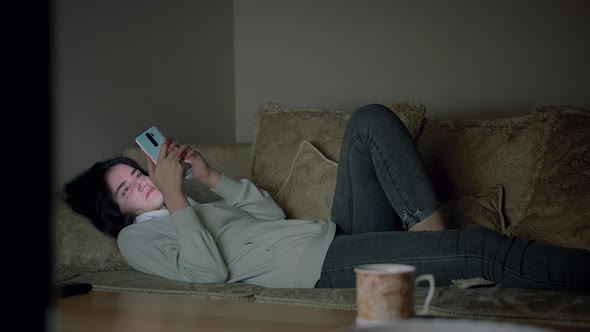 A Lonely Girl Spends the Evening Alone Lying on the Couch with a Mobile Phone