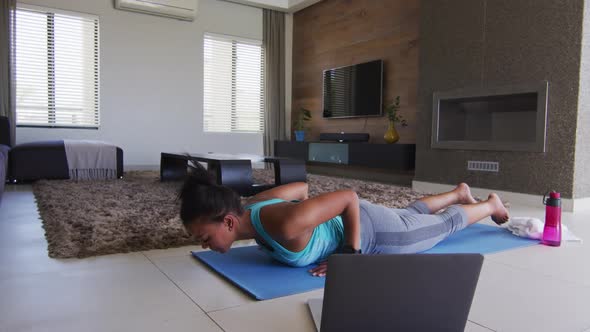 Mixed race woman excercising on a mat with laptop