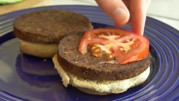 A vegan chef cooking and assembling two healthy tomato and avocado vegetarian burgers for lunch.