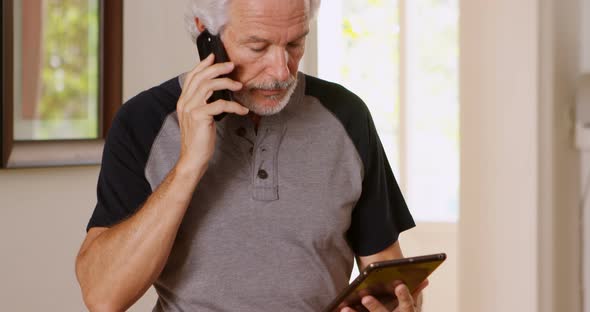Senior man talking on mobile phone while using digital tablet 4k