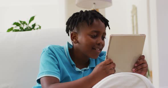 African american boy smiling while using digital tablet sitting on the couch at home