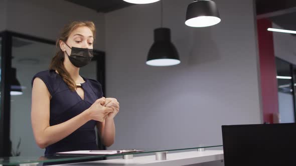 Caucasian woman in face mask disinfects hands and signs in at office reception desk