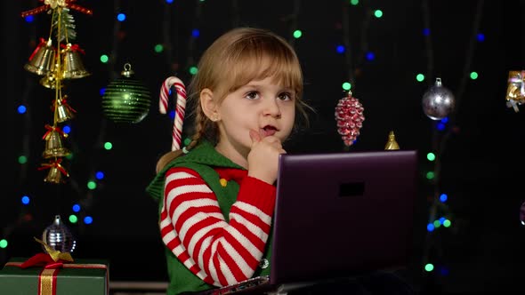 Kid Girl in Christmas Elf Costume Doing Shopping Online Using Laptop Browsing on Social Media