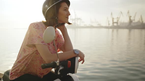 Young Beautiful Girl Sitting on Scooter Near Sea at Sunrise