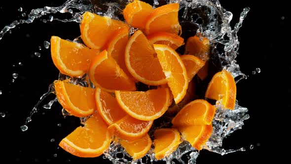 Super Slow Motion Shot of Rotating Exploded Orange Slices with Splashing Water on Black at 1000Fps