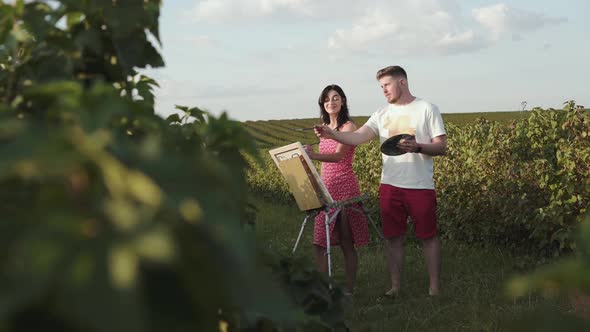 Cheerful Artists' Couple Discusses and Paints in the Summer Field