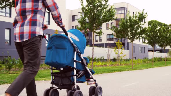 Father with Baby in Stroller Walking Along City