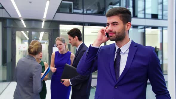 Businessman talking on mobile phone while businesspeople discussing in background