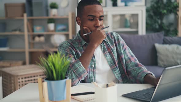 Tired, Stressed and Sleepy Freelance Worker African American Guy Is Using Laptop Working at Home