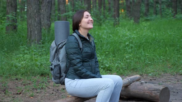 Happy Woman with Backpack Sitting on a Log in the Forest