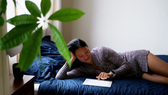 Woman using digital tablet while relaxing on bed