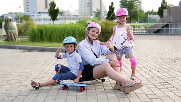 Mom and Kids Sit on a Skateboard and Give a Thumbs Up