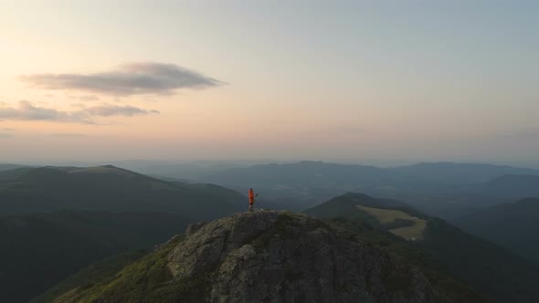 Young Man Hiker Sitting on Rocky Mountain Reading Map with Sunset Sky and Deep Valley Below