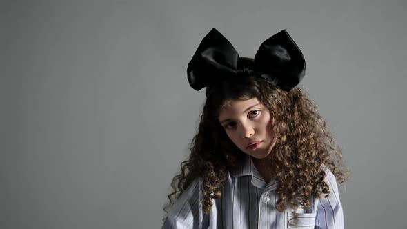 Tired young girl rubbing eyes, with large black bow in hair