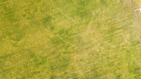 Top down aerial view of football field surface covered with green grass and sprinklers spraying