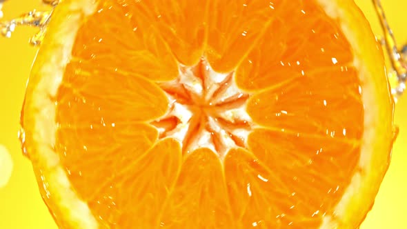 Super Slow Motion Detail Shot of Rotating Fresh Orange Slice and Splashing Water at 1000Fps