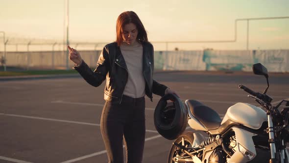 Beautiful Young Redhaired Woman Motorcyclist Dancing Next to Her Custom Bike with Black Motorcycle