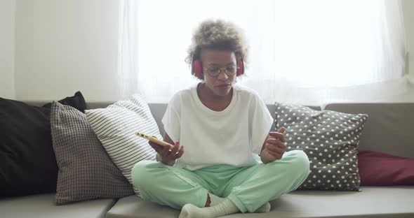 Smiling African American Woman Listening to Music and Dancing on a Sofa at Home