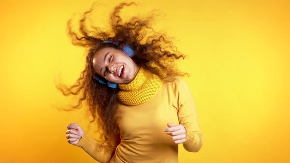 Attractive Woman with Blue Headphones Dancing Isolated on Yellow Background