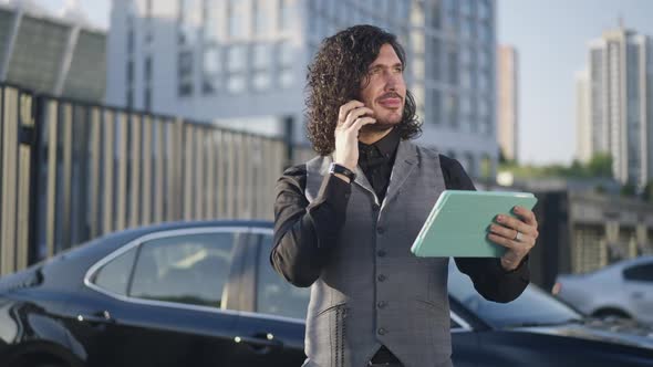 Portrait of Confident Intelligent Young Businessman Standing at Car Downtown Talking on Phone