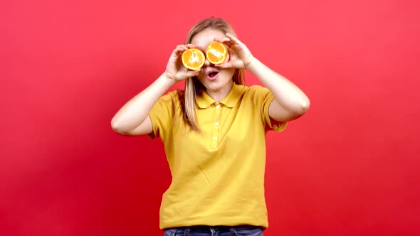 Happy, Optimistic Girl in a Yellow T-shirt, Covering Her Eyes with Tangerines and Showing Her Tongue