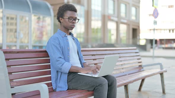 Young African Man with Laptop Looking at Camera While Sitting Outdoor on Bench