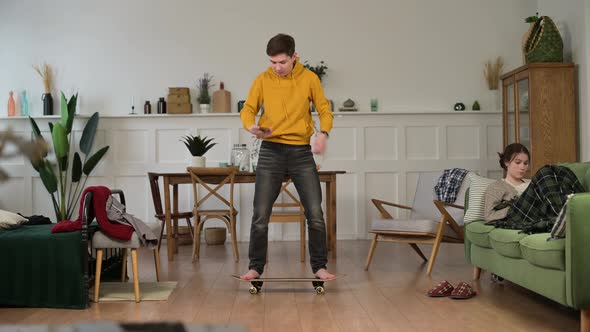 A young guy fooling around at home and learning to stand on a skateboard, then falling