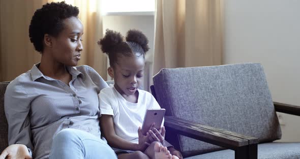 Little Girl Daughter Afro American Black Ethnic Child Sits Near Mother Holds Modern Gadget