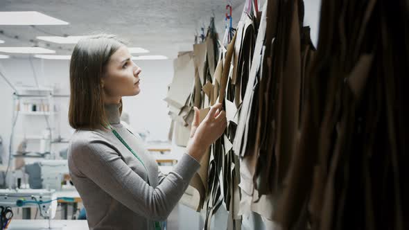 Young Female Fashion Designer or Tailor of Sewing Workshop is Choosing a Pattern or Mold Hanging on
