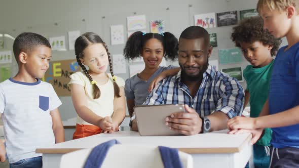 Video of happy african american male teacher and class of diverse pupils working on tablet