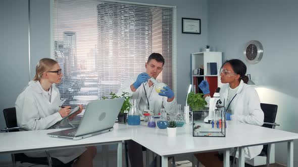 Diverse Team of Research Scientists Observing Collegue's Experiment with Liquid in Conical Flask alt
