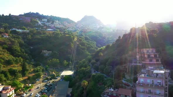 Flying towards the cable-car station located between green hills. Taormina-Mazzaró route, Italy; cam