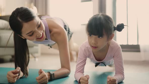 Funny cute little kid daughter meditating in lyoga with asian young mom at home