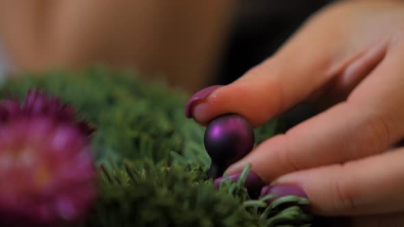Woman making a fir Advent wreath for Christmas Eve and decorating it with small purple ball, diy cra