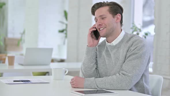 Serious Creative Young Man Talking on Smartphone in Office 