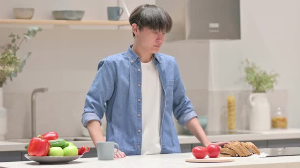 Serious Young Asian Man Thinking While Standing in Kitchen