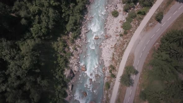 Aerial top down shot of a turquoise glacier river flowing between the forest in Venosc, French Alps.