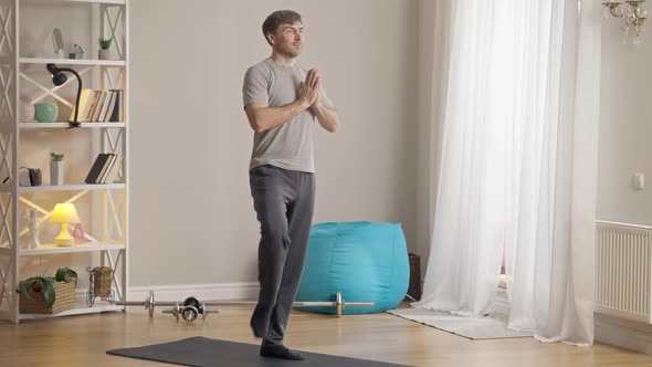 Wide Shot Portrait of Calm Confident Sportsman Standing in Tree Pose on Exercise Mat Indoors