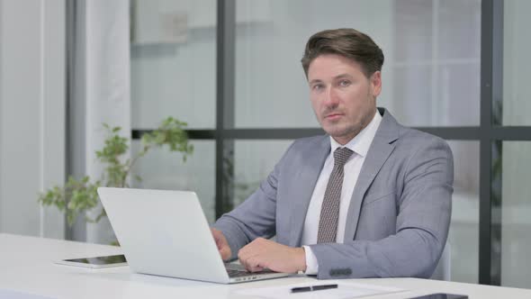 Middle Aged Man Shaking Head as No Sign while using Laptop in Office
