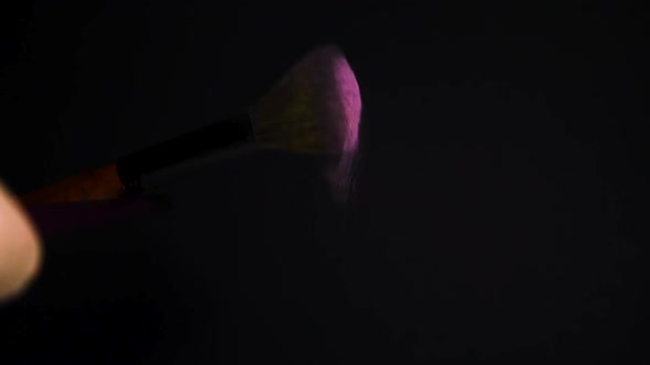 slow motion of a make up brush with pink powder explosion and burst on black background