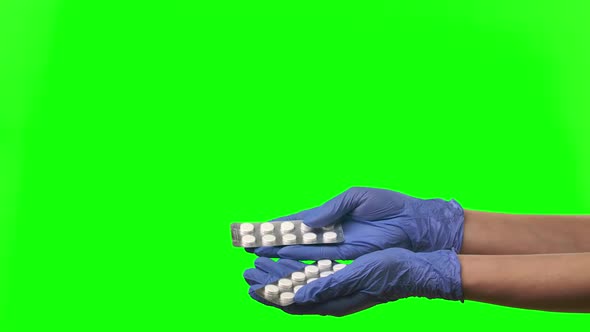 Doctor Shows Pills. Female Hands in Protective Blue Gloves Closeup at Green Screen.