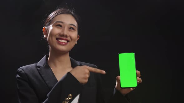 Speaker Woman In Business Suit Holding And Pointing Green Screen Smartphone In The Black Studio